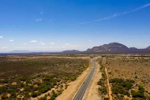 Aerial view of a long road stretching through the arid landscape of Marsabit County with scattered trees and distant mountains in Marsabit Marsabit County Kenya. Aerial view of a long road stretching through the arid landscape of Marsabit County with scattered trees and distant mountains in Marsabit Marsabit County Kenya.