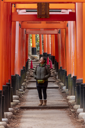 View of a woman standing under the Senbon Torii gates at Fushimi Inari Shrine surrounded by vibrant orange structures and stone bases Kyoto Kyoto Japan.