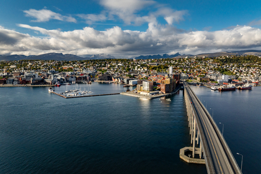 Aerial view of Tromso Bridge connecting the city center with the mainland featuring the harbor colorful buildings and surrounding mountains under a cloudy sky in Tromso Troms Norway.