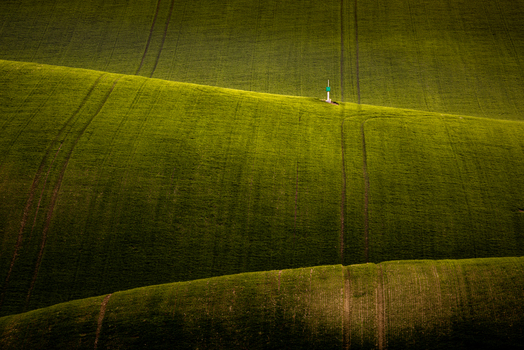 View of rolling green agricultural hills with tractor tracks and a small marker on a ridge in Cejkovice South Moravian Region Czechia. View of rolling green agricultural hills with tractor tracks and a small marker on a ridge in Cejkovice South Moravian Region Czechia.
