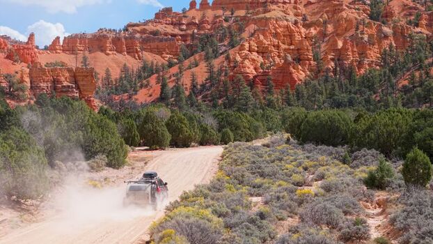 Aerial view of an SUV pulling a teardrop camper trailer along a dusty dirt road through the red rock landscape of Costa Canyon in Panguitch Utah United States.