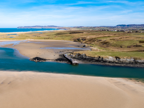 Aerial view of Ballyness Bay featuring a sandy tidal inlet a small pier extending into the water and the surrounding green coastal landscape in Ballyness County Donegal Ireland. Aerial view of Ballyness Bay featuring a sandy tidal inlet a small pier extending into the water and the surrounding green coastal landscape in Ballyness County Donegal Ireland.