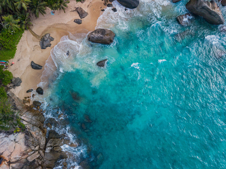 Aerial view of turquoise waves crashing against the sandy shore fringed by verdant trees and scattered rocks Vista do Mar Seychelles. Aerial view of turquoise waves crashing against the sandy shore fringed by verdant trees and scattered rocks Vista do Mar Seychelles.