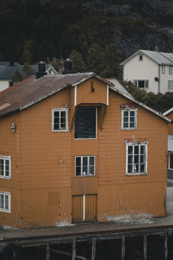 Nusfjord Norway 07 September 2022 View of the historic yellow wooden building in Nusfjord featuring weathered siding white framed windows and a rustic pier. Nusfjord Norway 07 September 2022 View of the historic yellow wooden building in Nusfjord featuring weathered siding white framed windows and a rustic pier.