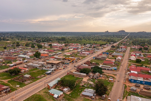 Aerial view of Katakwi Town Council with a main road stretching through the town scattered buildings lush green vegetation and a distant rocky hill in Katakwi Eastern Region Uganda. Aerial view of Katakwi Town Council with a main road stretching through the town scattered buildings lush green vegetation and a distant rocky hill in Katakwi Eastern Region Uganda.