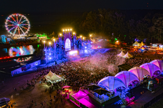 Herzogenaurach Germany 22 July 2022 Aerial view of the Open Beatz Festival featuring a large illuminated main stage a glowing Ferris wheel and a dense crowd of people at night. Herzogenaurach Germany 22 July 2022 Aerial view of the Open Beatz Festival featuring a large illuminated main stage a glowing Ferris wheel and a dense crowd of people at night.