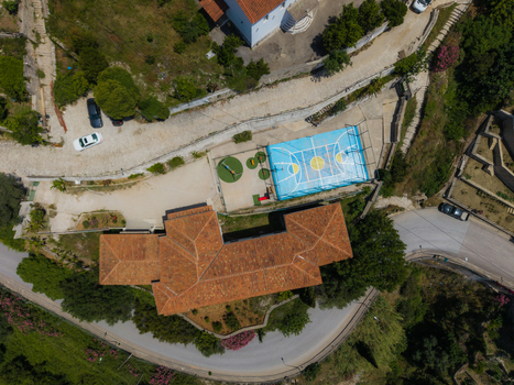 Aerial view of a building with a terracotta roof next to a blue basketball court and a small playground surrounded by winding roads and greenery in Dhermi Vlore County Albania. Aerial view of a building with a terracotta roof next to a blue basketball court and a small playground surrounded by winding roads and greenery in Dhermi Vlore County Albania.