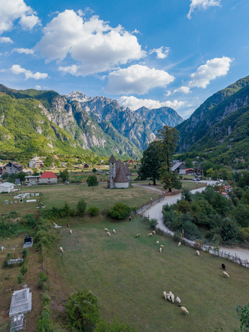 Aerial view of the historic stone church in the valley of Theth surrounded by grazing sheep and dramatic mountain peaks in Theth Shkoder County Albania. Aerial view of the historic stone church in the valley of Theth surrounded by grazing sheep and dramatic mountain peaks in Theth Shkoder County Albania.