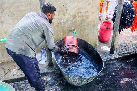 Narayanganj Bangladesh 29 March 2026 View of a worker in gloves pouring water into a tub of indigo dye creating a striking contrast against the weathered wall. Narayanganj Bangladesh 29 March 2026 View of a worker in gloves pouring water into a tub of indigo dye creating a striking contrast against the weathered wall.