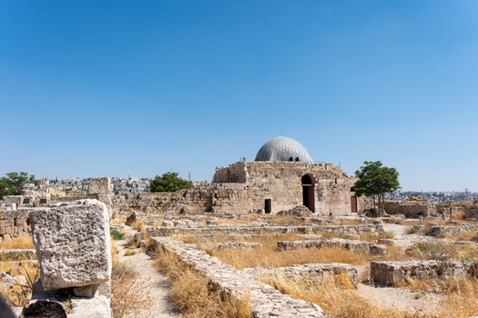 View of the Umayyad Palace with its iconic dome surrounded by ancient stone ruins and dry grass under a clear blue sky in Amman Amman Governorate Jordan.