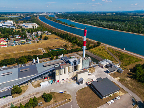 Aerial view of Glas Trosch Alsace SAS industrial facility with a tall red and white chimney large factory buildings and storage silos next to a canal in Hombourg Grand Est France.