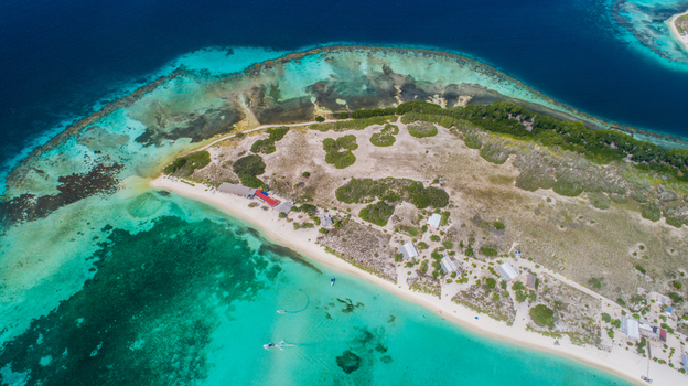 Aerial view of Los Roques archipelago featuring turquoise waters coral reefs a sandy beach and small structures on the island in Los Roques Dependencias Federales Venezuela. Aerial view of Los Roques archipelago featuring turquoise waters coral reefs a sandy beach and small structures on the island in Los Roques Dependencias Federales Venezuela.