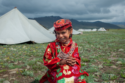 Skardu Gilgit Baltistan Pakistan 20 July 2010 View of a young girl in traditional red clothing sitting near tents in the grassy landscape of Deosai Top.