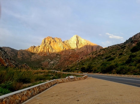 View of the rugged mountains in the Cogmans Kloof pass with golden sunlight hitting the peaks a paved road and stone retaining walls in Montagu Western Cape South Africa.