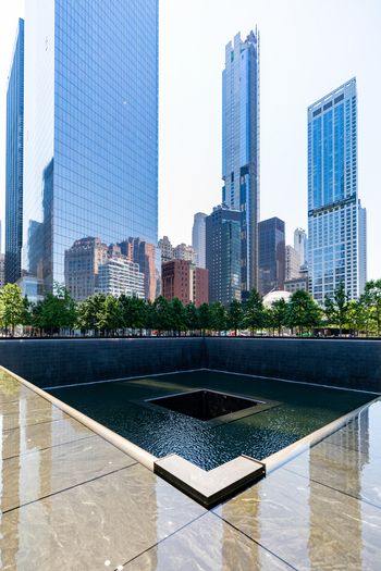 View of the 911 Memorial reflecting pool surrounded by modern skyscrapers and lush trees in the financial district of New York New York United States. View of the 911 Memorial reflecting pool surrounded by modern skyscrapers and lush trees in the financial district of New York New York United States.