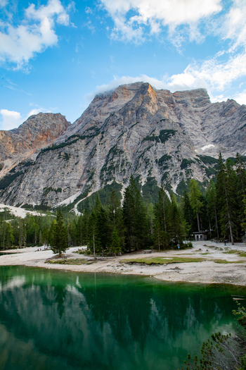 View of the Dolomites mountain range reflecting in the emerald green waters of the lake surrounded by dense pine forests and rocky shores in Rocca Pietore Veneto Italy. View of the Dolomites mountain range reflecting in the emerald green waters of the lake surrounded by dense pine forests and rocky shores in Rocca Pietore Veneto Italy.