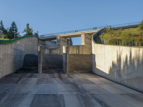 Aerial view of the concrete spillway of the earth dam on Czorsztyn Reservoir with a pedestrian bridge above and grassy slopes under a clear blue sky in Niedzica Malopolskie Poland.