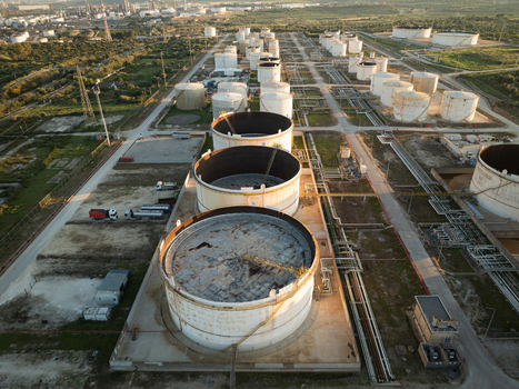 Aerial view of large industrial storage tanks and refinery infrastructure surrounded by green fields in Augusta Sicily Italy. Aerial view of large industrial storage tanks and refinery infrastructure surrounded by green fields in Augusta Sicily Italy.