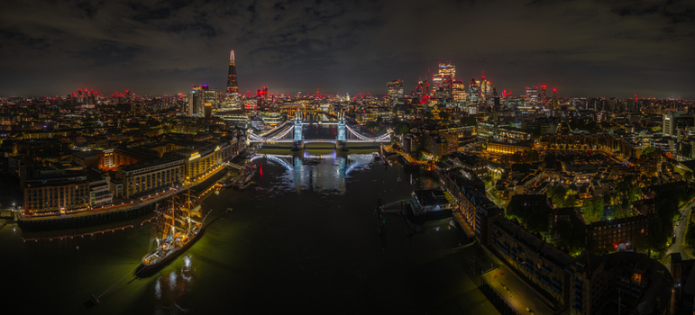 Aerial view of the illuminated Tower Bridge and the City of London skyline at night with the River Thames flowing through the urban landscape London England United Kingdom.