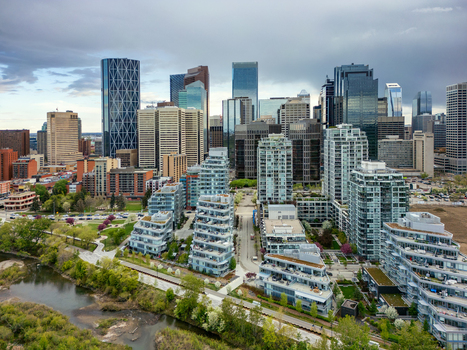 Aerial view of the Calgary skyline featuring modern glass skyscrapers residential apartment complexes and the Bow River under a cloudy sky in Calgary Alberta Canada.