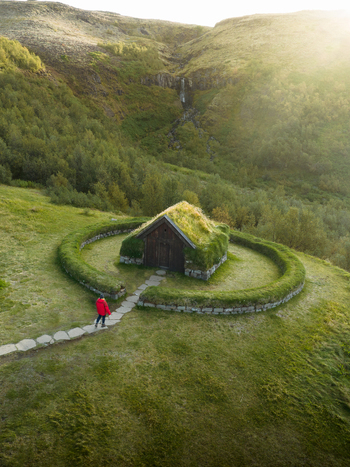 Aerial view of a lone figure walks towards the turf roofed church surrounded by a circular stone wall nestled within the verdant Icelandic landscape Selfoss Skeiða og Gnúpverjahreppur Iceland. Aerial view of a lone figure walks towards the turf roofed church surrounded by a circular stone wall nestled within the verdant Icelandic landscape Selfoss Skeiða og Gnúpverjahreppur Iceland.