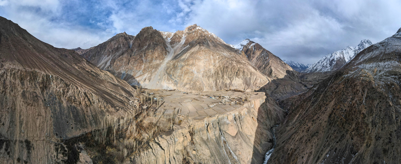 Aerial view of rugged mountains with snow capped peaks and a village nestled on a plateau Chapursan Valley Hunza Nagar Pakistan. Aerial view of rugged mountains with snow capped peaks and a village nestled on a plateau Chapursan Valley Hunza Nagar Pakistan.