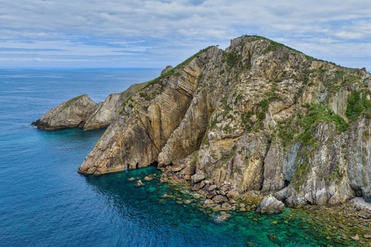 Aerial view of the Silence Beach Viewpoint featuring dramatic rocky cliffs and turquoise waters under a cloudy sky in Cudillero Asturias Spain.