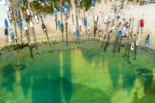 Aerial view of numerous small fishing boats pulled onto the sandy beach with wooden slipways extending into the clear green water in Saints Constantine and Helena Varna Bulgaria.