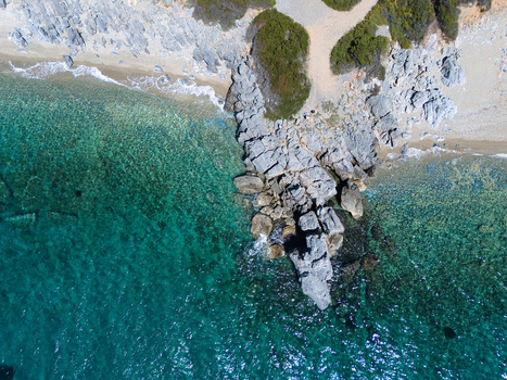 Aerial view of a pebble beach and rocky coastline with turquoise clear water and green vegetation in Pallini Greece.