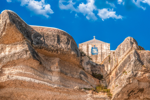 Aerial view of the Chapel of the Miracle s Memory nestled amidst the rugged sun kissed cliffs under a vibrant blue sky Nazar&eacute; Leiria Portugal.