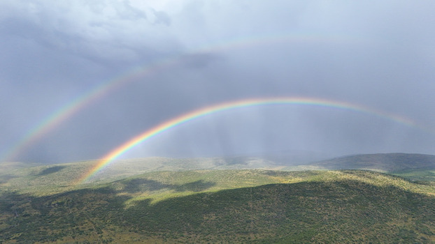 Aerial view of a double rainbow over rolling green hills and dense vegetation under a dramatic cloudy sky in Waterberg District Municipality Limpopo South Africa. Aerial view of a double rainbow over rolling green hills and dense vegetation under a dramatic cloudy sky in Waterberg District Municipality Limpopo South Africa.