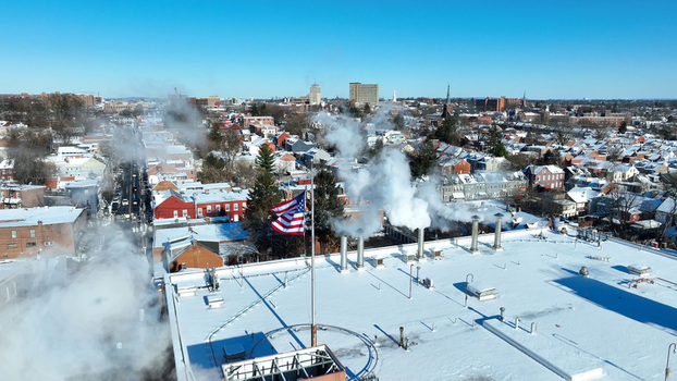 Aerial view of Lancaster in winter with snow covered rooftops steam rising from industrial vents and an American flag flying in the foreground Lancaster Pennsylvania United States.