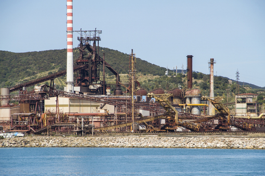 View of a sprawling industrial complex with towering chimneys and rusted metal structures meets the serene blue sea contrasting industry with nature Piombino Tuscany Italy. View of a sprawling industrial complex with towering chimneys and rusted metal structures meets the serene blue sea contrasting industry with nature Piombino Tuscany Italy.