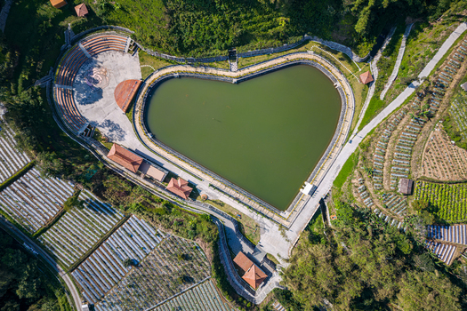 Aerial view of Embung Gumelem heart shaped reservoir and amphitheater surrounded by agricultural terraces and lush green hills in Pakis Central Java Indonesia.