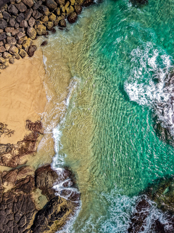 Aerial view of turquoise waters and rocky shoreline at Cudgen Headland South Head with waves crashing against dark volcanic rocks and sand in Kingscliff New South Wales Australia. Aerial view of turquoise waters and rocky shoreline at Cudgen Headland South Head with waves crashing against dark volcanic rocks and sand in Kingscliff New South Wales Australia.