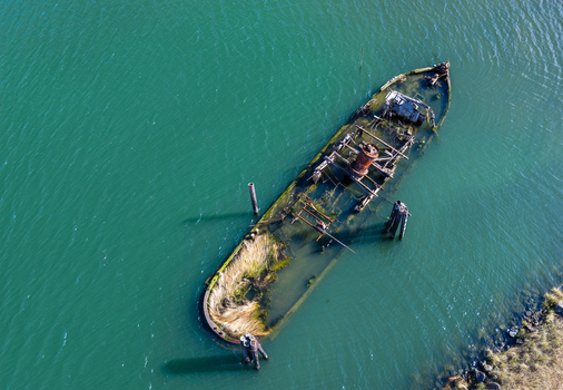 Aerial view of the historic Mary D. Hume shipwreck partially submerged in the Rogue River surrounded by calm green water in Gold Beach Oregon United States.