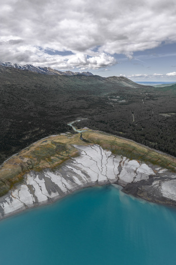 Aerial view of Alaska Wilderness featuring a turquoise glacial lake with silt banks dense evergreen forests and distant mountains under a cloudy sky in Eklutna Alaska United States. Aerial view of Alaska Wilderness featuring a turquoise glacial lake with silt banks dense evergreen forests and distant mountains under a cloudy sky in Eklutna Alaska United States.
