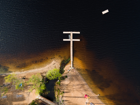 Aerial view of a wooden dock extending into the dark waters of Commanda Lake with a sandy shoreline and green trees in Restoule Ontario Canada. Aerial view of a wooden dock extending into the dark waters of Commanda Lake with a sandy shoreline and green trees in Restoule Ontario Canada.