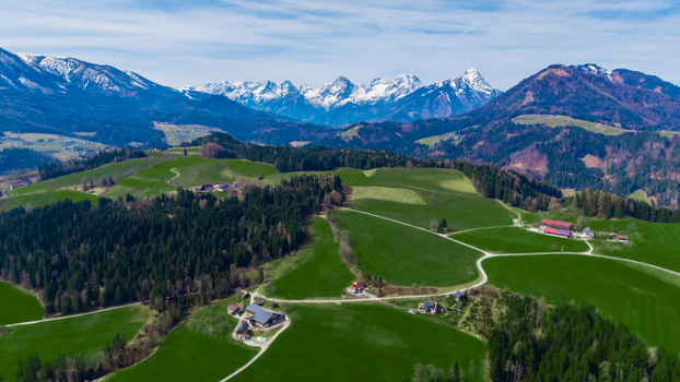 Aerial view of rolling green hills meeting dark forests crowned by snow capped mountains under a bright sky Windischgarsten Upper Austria Austria. Aerial view of rolling green hills meeting dark forests crowned by snow capped mountains under a bright sky Windischgarsten Upper Austria Austria.
