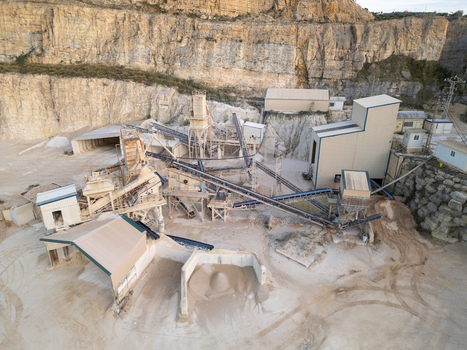 Aerial view of a stone quarry featuring industrial crushing machinery conveyor belts and storage areas set against a rocky cliff face in Teulada Valencian Community Spain.
