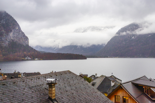 View of the historic rooftops of Hallstatt village overlooking the calm waters of Hallstatter See and misty alpine mountains in Hallstatt Upper Austria Austria. View of the historic rooftops of Hallstatt village overlooking the calm waters of Hallstatter See and misty alpine mountains in Hallstatt Upper Austria Austria.