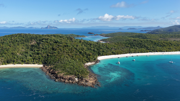 Aerial view of Whitehaven Beach with its pristine white sand turquoise waters lush green hills and sailboats anchored in the bay in Whitsundays Queensland Australia.