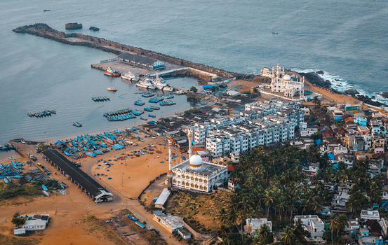 Aerial view of Vizhinjam harbor featuring numerous fishing boats a prominent mosque and coastal buildings along the shoreline in Kovalam Keralam India. Aerial view of Vizhinjam harbor featuring numerous fishing boats a prominent mosque and coastal buildings along the shoreline in Kovalam Keralam India.