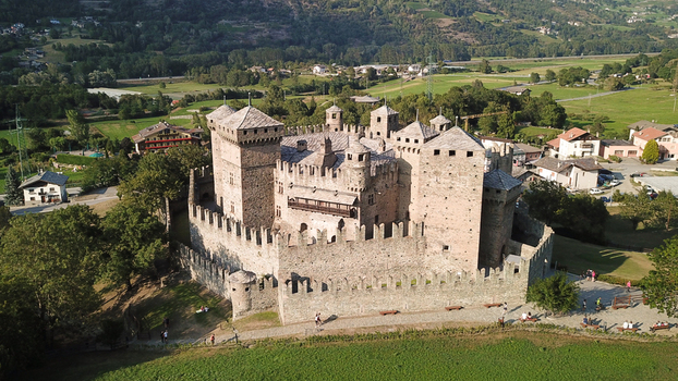 Aerial view of the historic Fenis Castle with its medieval stone towers and crenelated walls surrounded by green fields and trees in Aosta Valley Aosta Valley Italy. Aerial view of the historic Fenis Castle with its medieval stone towers and crenelated walls surrounded by green fields and trees in Aosta Valley Aosta Valley Italy.