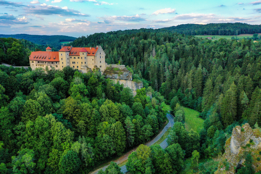 Aerial view of Burg Rabenstein castle perched on a cliffside surrounded by lush green forests and rolling hills Ahorntal Bayern Germany.