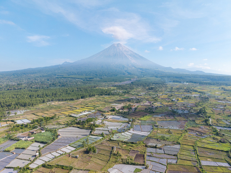 Aerial view of Sumberurip with lush rice paddies and forest landscape set against the volcanic peak of Mount Semeru in Pronojiwo East Java Indonesia. Aerial view of Sumberurip with lush rice paddies and forest landscape set against the volcanic peak of Mount Semeru in Pronojiwo East Java Indonesia.