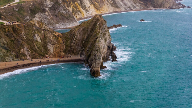 Aerial view of the natural limestone arch of Durdle Door on the Jurassic Coast with turquoise sea sandy beach and people walking on the coastal path in Wareham England United Kingdom. Aerial view of the natural limestone arch of Durdle Door on the Jurassic Coast with turquoise sea sandy beach and people walking on the coastal path in Wareham England United Kingdom.