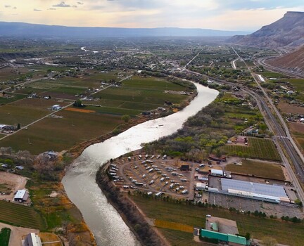 Aerial view of the winding river reflecting the bright sky flowing through the green fields and towards the distant mountains Palisade Colorado USA. Aerial view of the winding river reflecting the bright sky flowing through the green fields and towards the distant mountains Palisade Colorado USA.