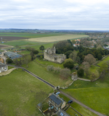 Aerial view of the medieval ruins of Dirleton Castle Gardens surrounded by lush green lawns and trees under an overcast sky in Dirleton Scotland United Kingdom. Aerial view of the medieval ruins of Dirleton Castle Gardens surrounded by lush green lawns and trees under an overcast sky in Dirleton Scotland United Kingdom.