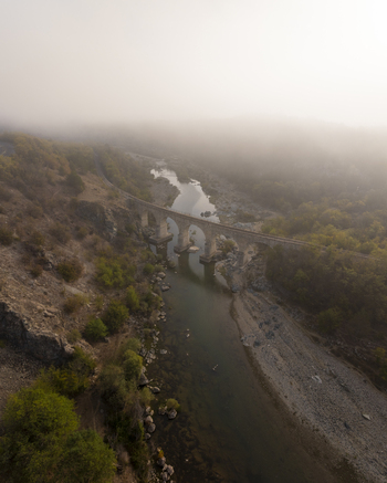 Aerial view of the historic stone railway bridge spanning a river in a misty valley surrounded by rocky hills and autumn trees in Balabanovo Kardzhali Province Bulgaria. Aerial view of the historic stone railway bridge spanning a river in a misty valley surrounded by rocky hills and autumn trees in Balabanovo Kardzhali Province Bulgaria.